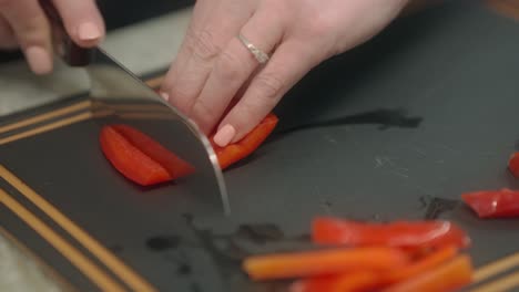 A-piece-of-red-pepper-being-slices-with-a-sharp-chef's-knife,-on-a-cutting-board