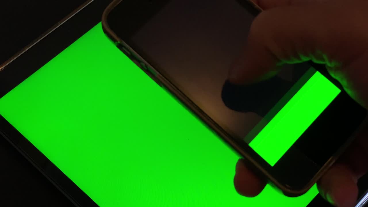 primer plano de un tipo negro que se desplaza por la pantalla táctil de un smartphone moderno, un dispositivo con una pantalla de tecla de croma verde y una tableta verde en segundo plano