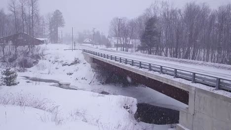 Luftaufnahme-In-Zeitlupe,-Die-Sich-Einer-Brücke-Nähert,-Die-Während-Eines-Schneesturms-über-Einen-Eisigen-Fluss-Führt