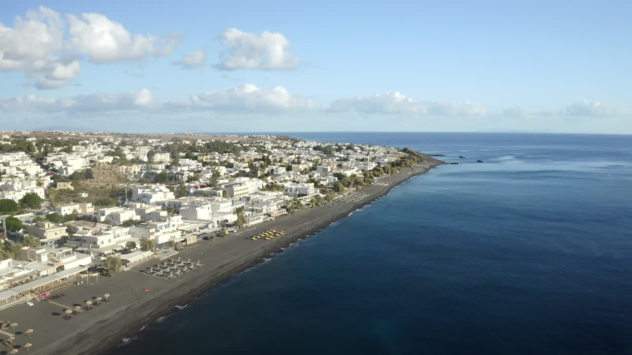 toma aérea de drones volando sobre la playa de arena negra en la isla griega de santorini, con tumbonas y agua de mar azul en 4k
