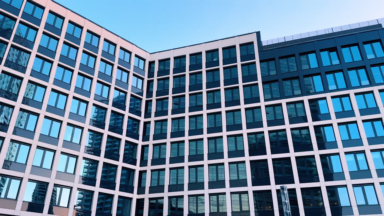 Bratislava, Slovakia - June 5, 2025: Urban building with glass windows. Reflective windows of a contemporary building capture nearby structures under a clear blue sky in an urban setting