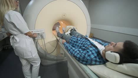 mujer médico hace escaneo de resonancia magnética de la articulación de la rodilla. joven paciente en la mesa automática entra en una máquina de resonancia eléctrica de tipo cerrado usando auriculares de aislamiento de ruido. equipo moderno, bobina en la rodilla del paciente