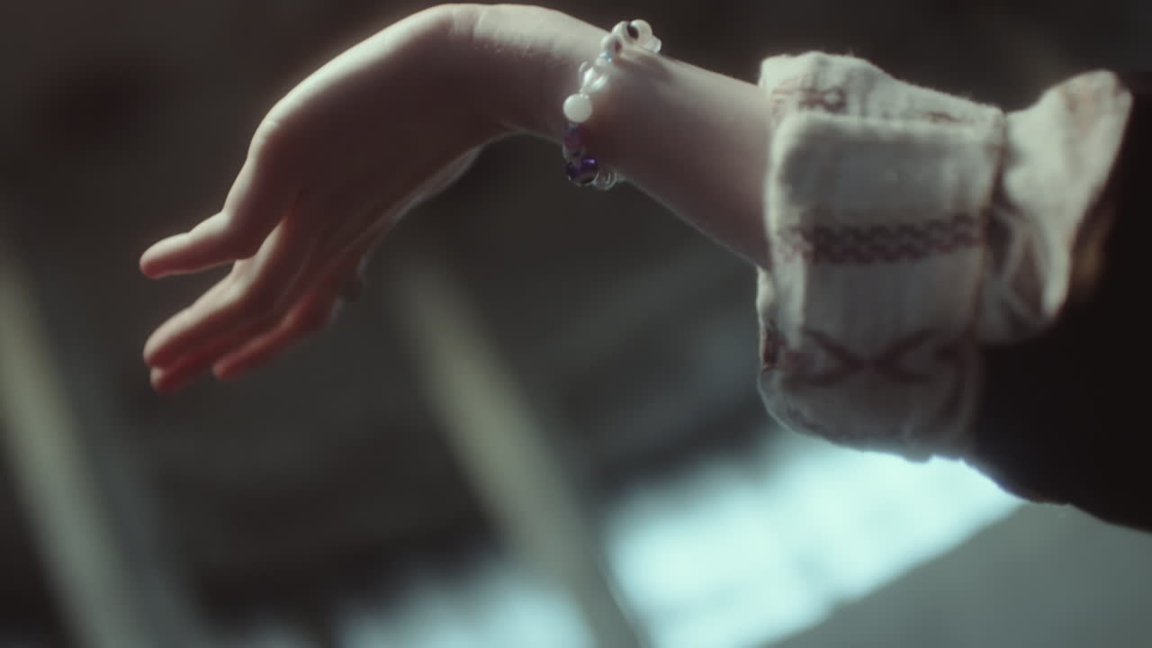 A hand adorned with a bracelet and ring reaches out in soft focus