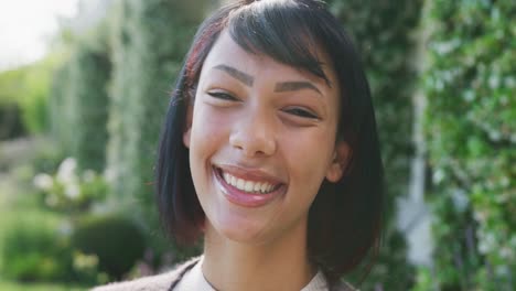 retrato de una adolescente biracial feliz mirando a la cámara y sonriendo en el jardín, en cámara lenta
