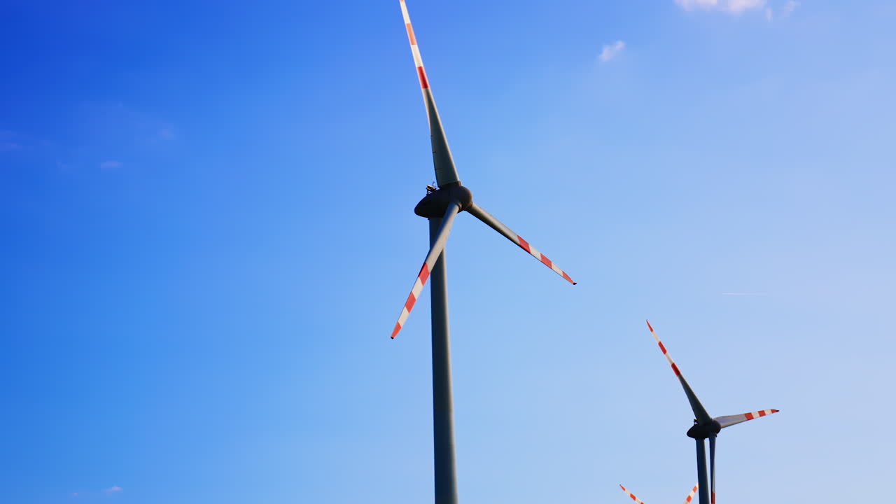 Wind turbines under a clear blue sky. Two wind turbines with red and white stripes stand tall against a vibrant blue sky, harnessing renewable energy