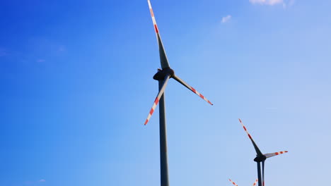 wind turbines under a clear blue sky. two wind turbines with red and white stripes stand tall against a vibrant blue sky, harnessing renewable energy