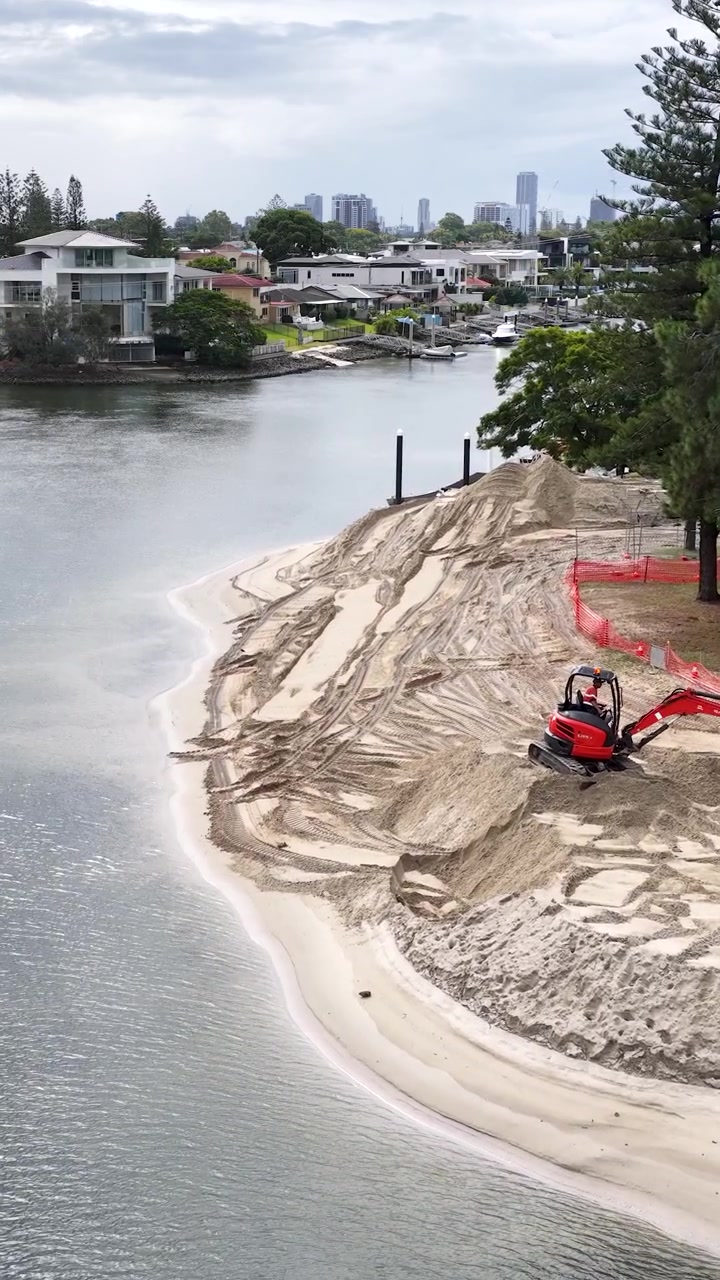 Un escavatore rosso sposta sabbia per il ripristino della spiaggia lungo un canale suburbano della Gold Coast