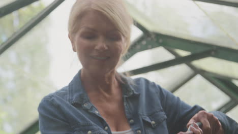 mature woman with watering can gardening in greenhouse at home