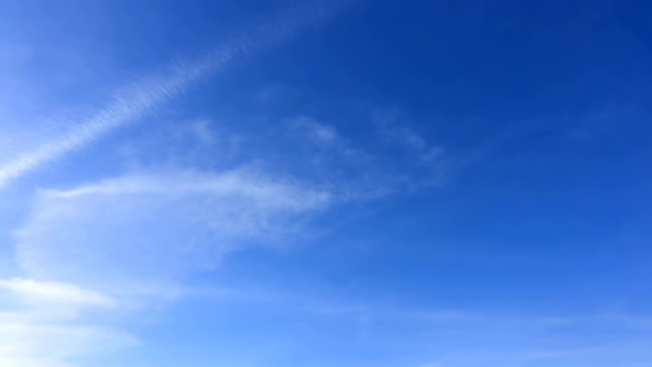 Un cielo azzurro limpido riempie l'inquadratura con soffici nuvole leggere che fluttuano nella luce del giorno, creando uno sfondo naturale calmo e arioso.