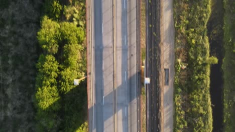 aerial top down dolly in following a road and railway cable-stayed bridge surrounded by vegetation at golden hour