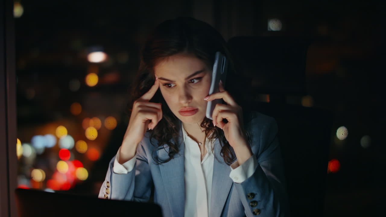 Confused businesswoman speaking smartphone in office late evening. Tired lady