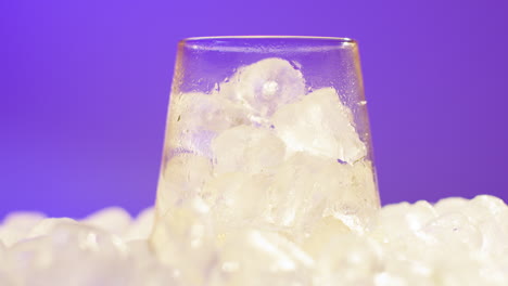 Nahaufnahme-Einer-Person,-Die-Gekühltes-Kaltgetränk-Aus-Der-Dose-Auf-Eiswürfel-Vor-Violettem-Hintergrund-In-Ein-Glas-Gießt