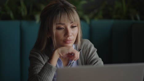 retrato de una hermosa joven y atractiva mujer asiática está sentada y parece preocupada y seria mientras reflexiona frente a su computadora portátil durante el día.