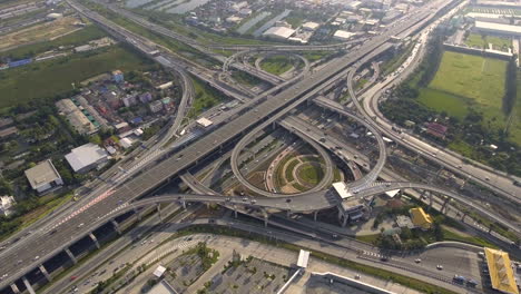 Vista-Aérea-Del-Cruce-De-Carreteras-Con-Tráfico-Urbano-Intenso-Acelerando-En-La-Carretera