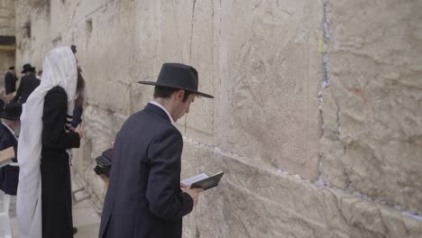 jewish prayer at western wall, jerusalem, israel. religious men rock backwards and forwards and side to side while praying. some wear black suits and hats. others wear while shawls and phylacteries.