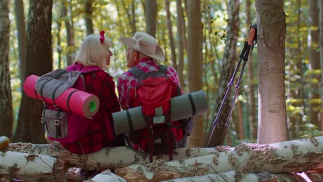 Grandmother-grandfather-senior-tourists-hikers-sitting-on-tree-and-hugging,-kissing-in-summer-forest