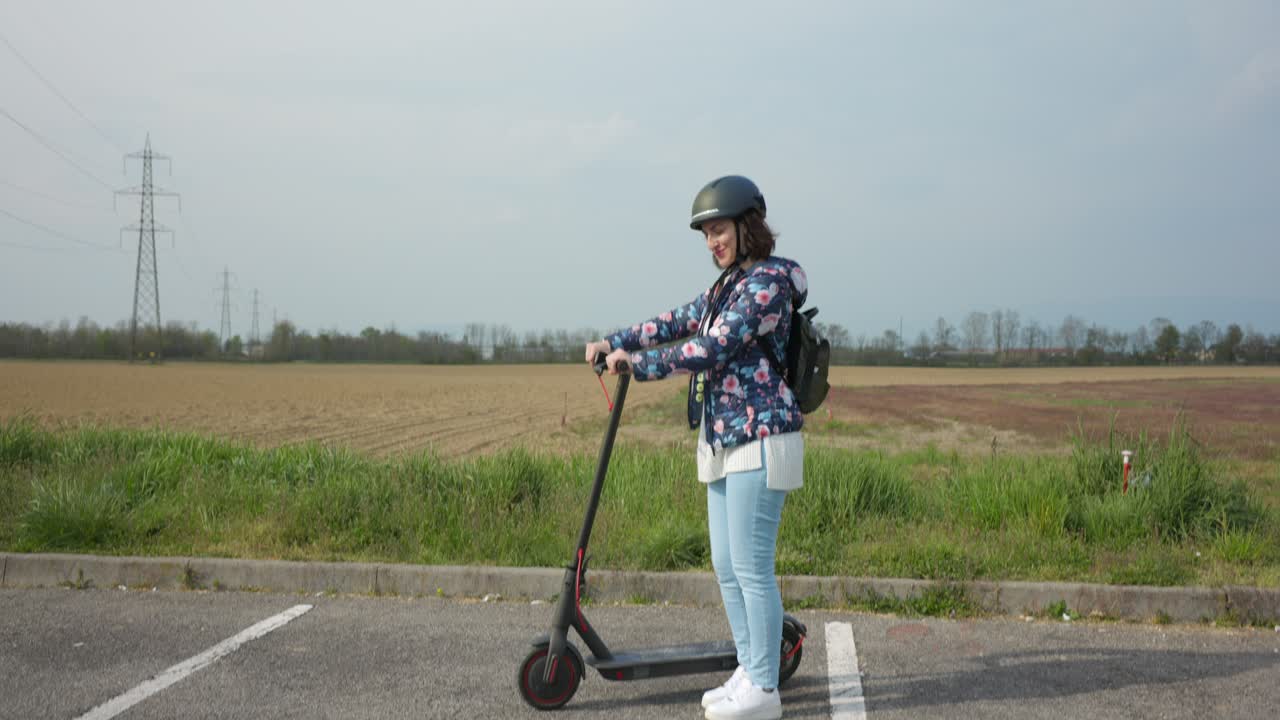 Aşağıya doğru kaydırma, kask takan kadın elektrikli scooter'ını çalıştırmaya başlıyor.