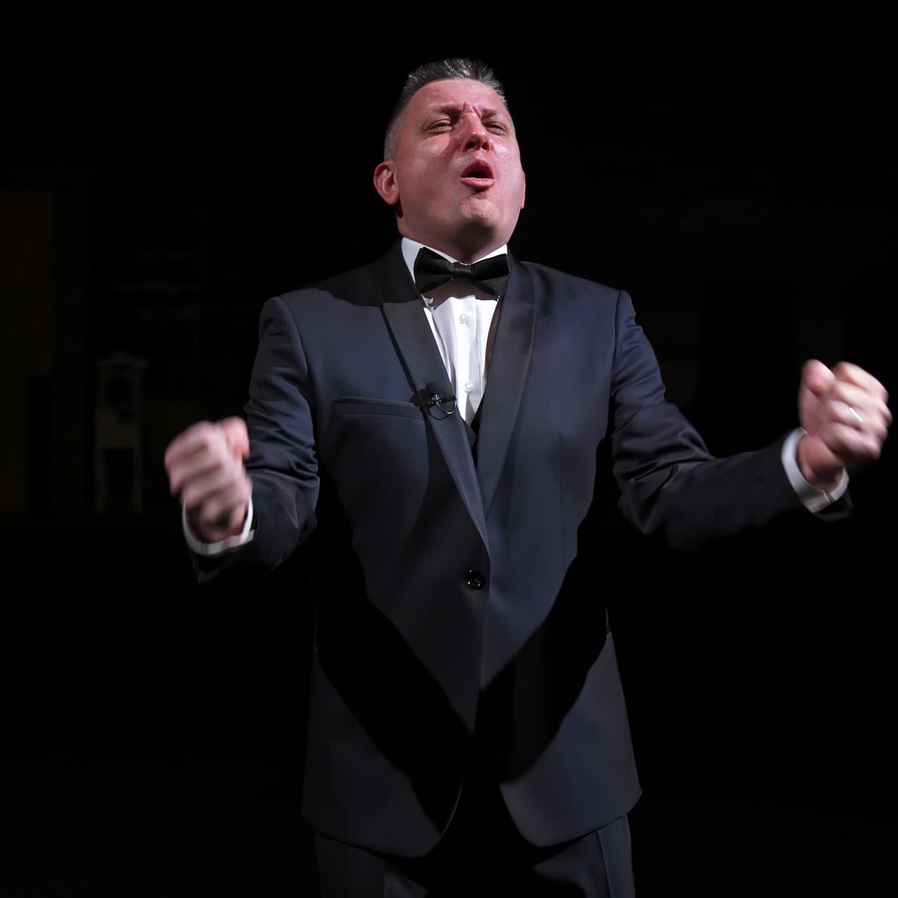 Man is speaking in the light of the floodlights standing on stage to the camera. Actor, artist on performance. Activ gestures with hands