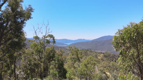 Rising-cinematic-drone-shot-of-mountains-and-blue-water-and-green-trees-near-Lake-Eildon,-Victoria-Australia