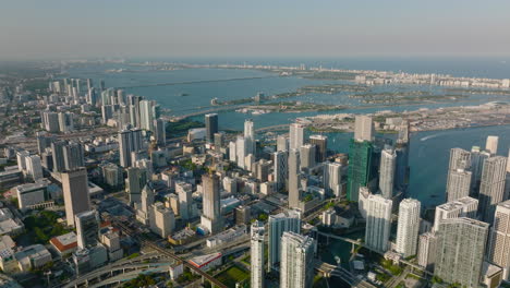 Amazing-aerial-footage-of-modern-high-rise-buildings-in-city-lit-by-late-afternoon-sun.-Sea-bay-with-islands-in-background.-Miami,-USA