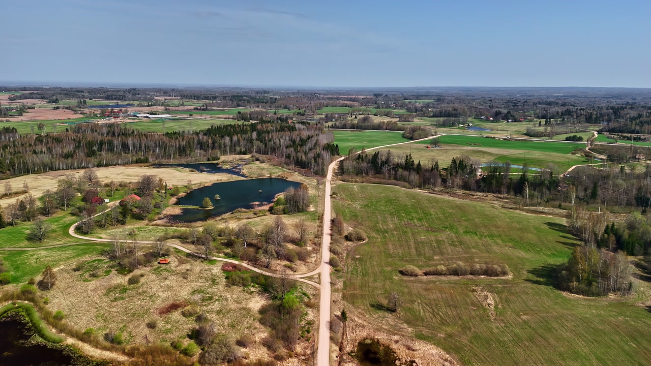 Drone view of rural farmland with a country road, fields, tree lines and small lakes. Aerial countryside scene with open land, spring colors and peaceful agricultural landscape.