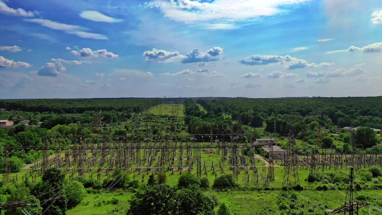 High voltage line among fields. Electric supports against the sky among green nature. Power transmission lines in summer. Aerial view.