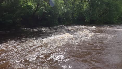 Panning-shot-of-a-murky-brown-river-with-its-banks-flooded-to-dangerous-levels