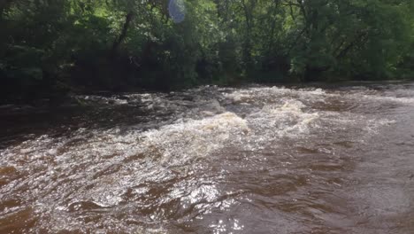 panning shot of a murky brown river with its banks flooded to dangerous levels