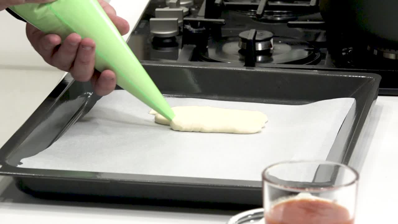 A person is carefully piping bright green batter onto parchment paper in a sleek kitchen. The process showcases an exciting method for preparing delicious desserts