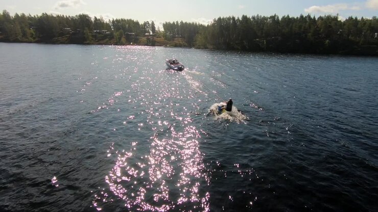 Slowmotion of a Drone flying over a young man riding a wakeboard after a sport boat in the Swedish archipelago in the summer sub5