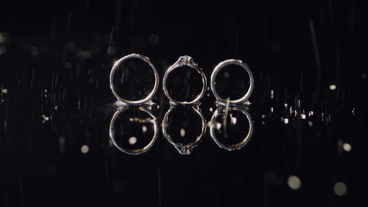 결혼과 약혼 반지는 어두운 물 표면에 누워 빛으로 빛나고 있습니다.