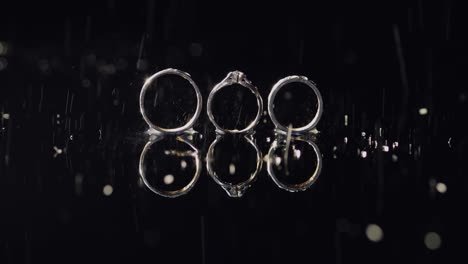 wedding and engagement rings lying on dark water surface shining with light