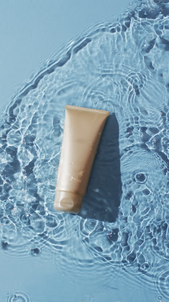 Video verticale di tubetto di prodotto di bellezza nell'acqua con spazio per la copia su sfondo blu