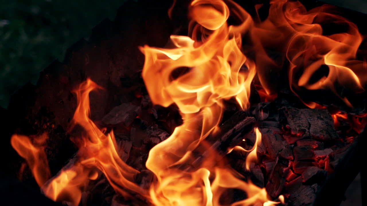 Orange flame on black firewood. Bright fire burning on black background outdoor. Detailed motion of burning logs.
