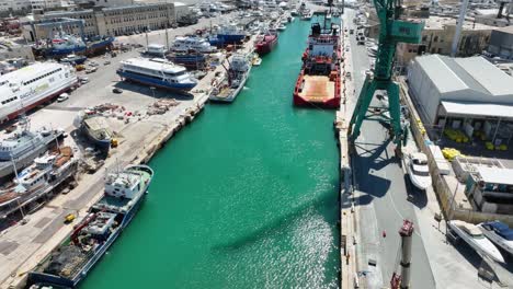 Aerial-drone-shot-flying-low-over-blue-seas-near-revealing-many-boats-and-ships-in-a-very-busy-boat-yard