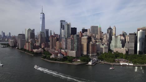 Aerial-view-of-ferries-in-front-of-lower-Manhattan,-summer-in-New-York,-USA---rotating,-pull-back,-drone-shot