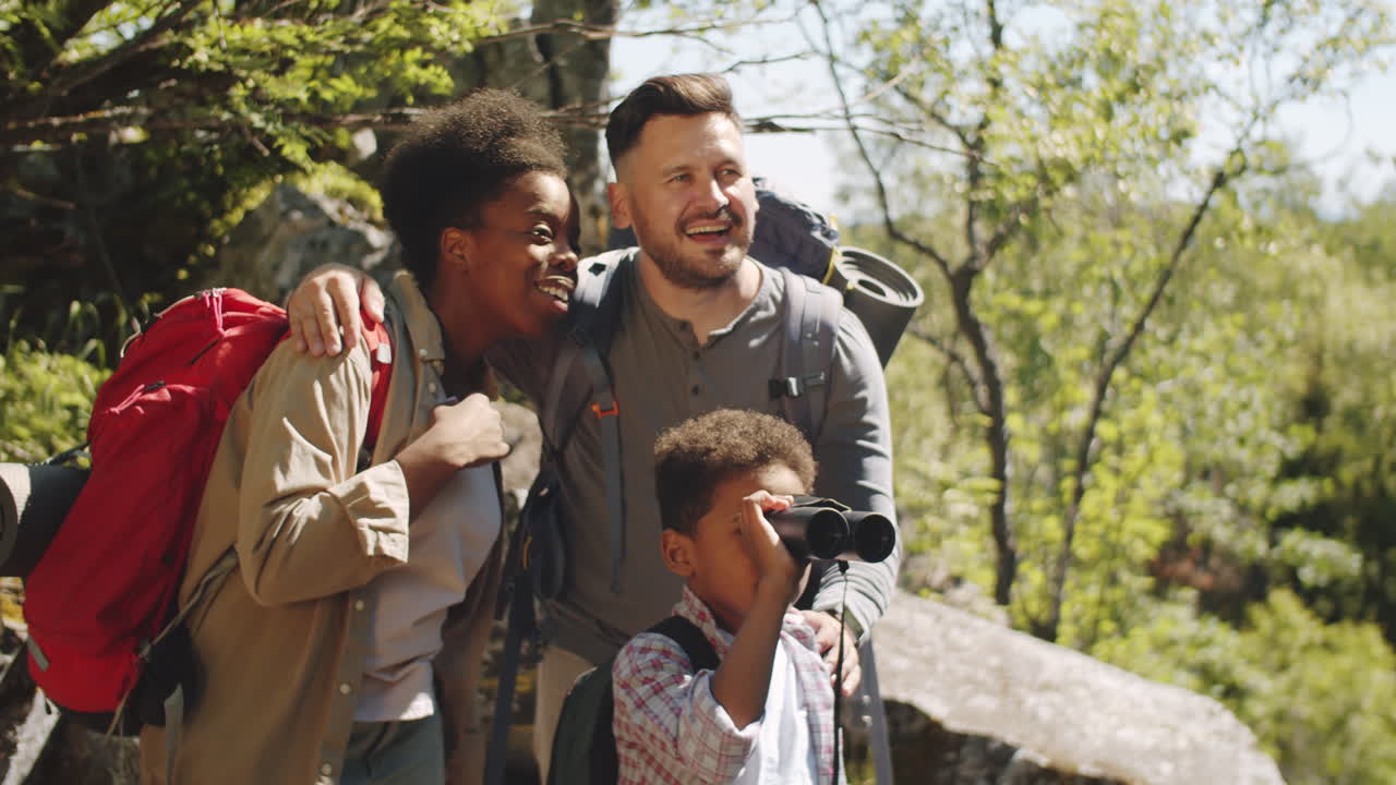 familia multiétnica usando binoculares mientras hacen senderismo en la naturaleza
