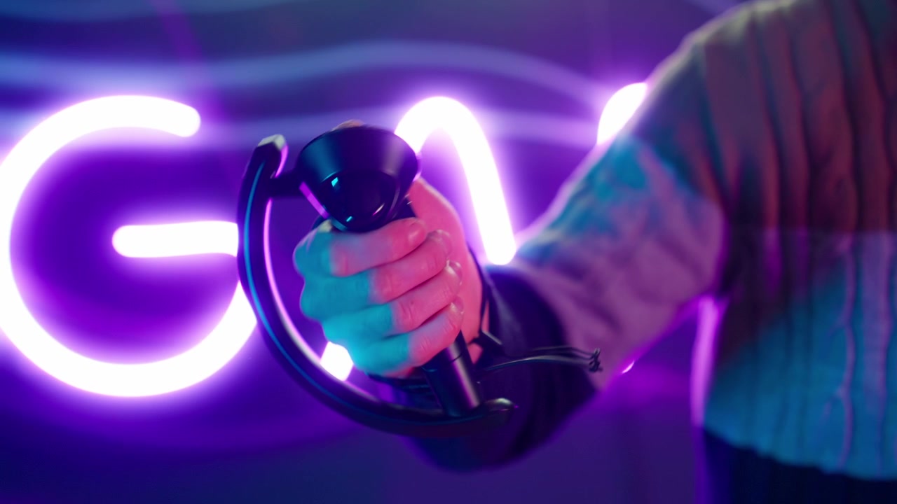 Primo piano di una mano che impugna un controller VR in un ambiente di gioco illuminato al neon.