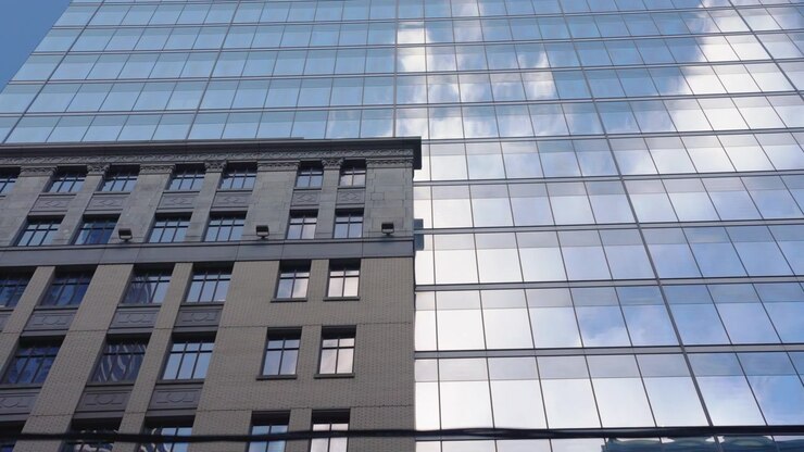 Edificio storico in pietra contrasta con una torre per uffici in vetro riflettente mentre la telecamera si sposta da sinistra a destra con nuvole riflesse sulla facciata in vetro