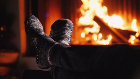 Beine-In-Socken-In-Der-Nähe-Des-Kamins,-Wo-Das-Feuer-Abends-Am-Feuer-Brennt