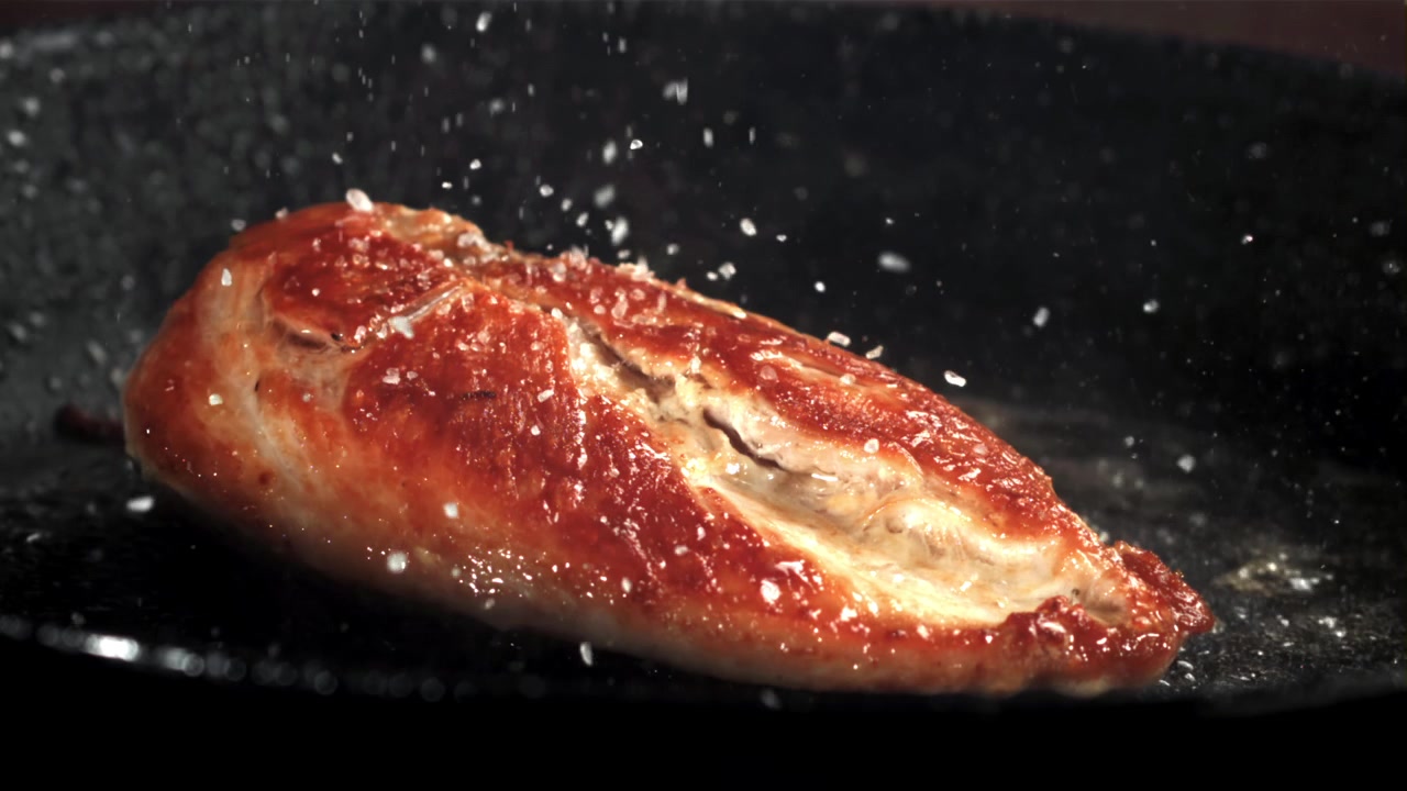 Slowmotion: Salt drysses på gyldenbrun kylling på stegepande