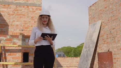 female architect in business attire stands in a newly built house with untreated walls and works on a tablet. modern technologies in the oldest professions