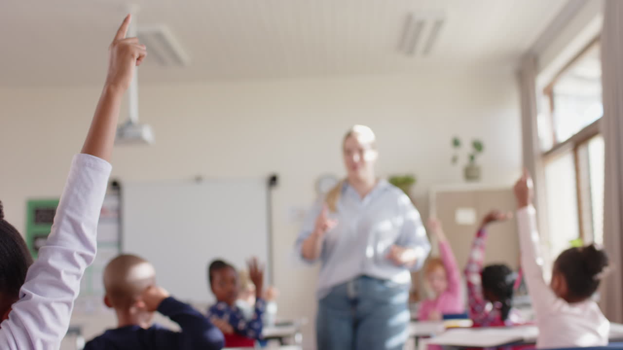 In school classroom, students raising hands while female teacher engaging with them