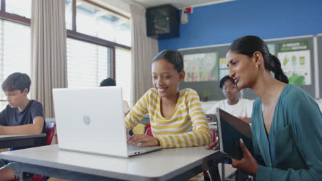 helping student using laptop in classroom, teacher collaborating on school project