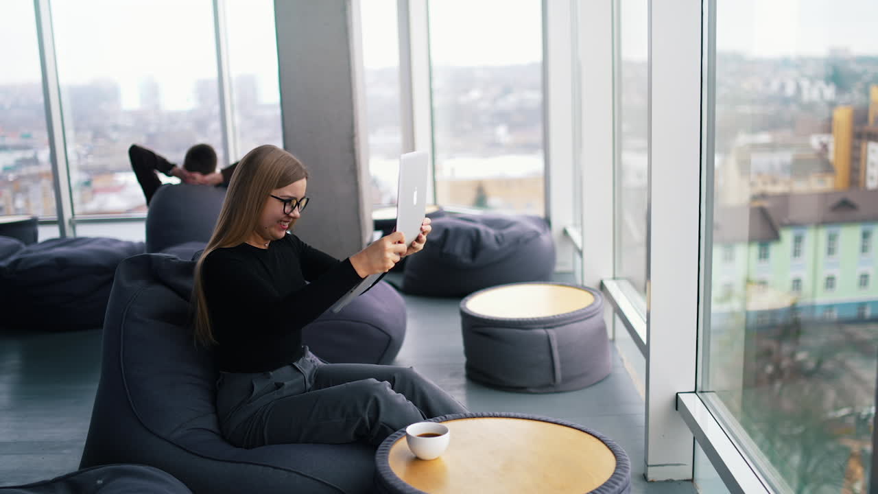 Business woman with a notebook sits in office. Female office worker has some problems with a laptop and shaking it. Faulty device in woman's hands.