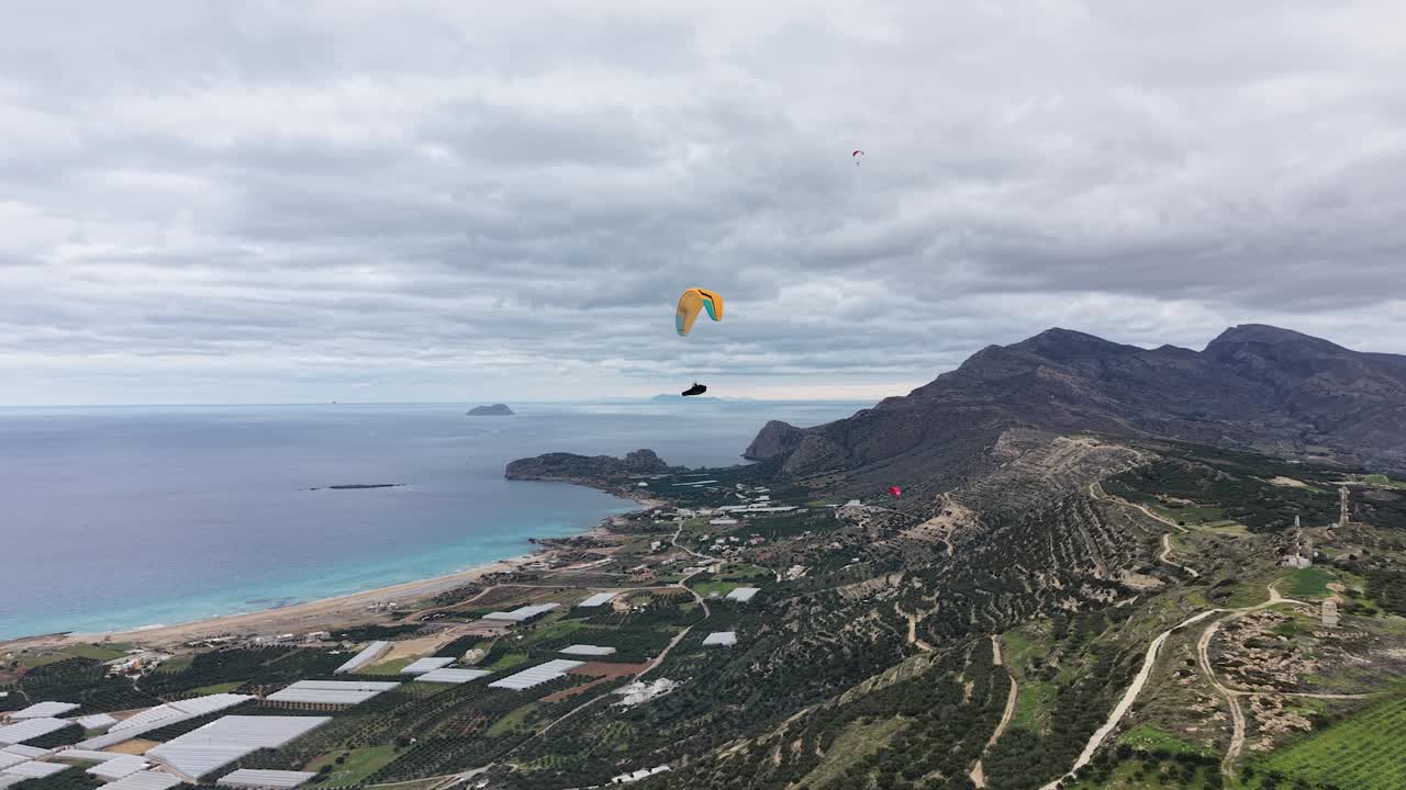 Ripresa aerea con drone di due parapendisti che scendono verso una valle, con montagne e il mare sullo sfondo. Paesaggio costiero suggestivo che esprime avventura, libertà e viaggi all'aria aperta.