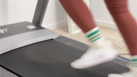 a woman exercises on a treadmill, monitoring her heart rate in a well-lit home gym setting