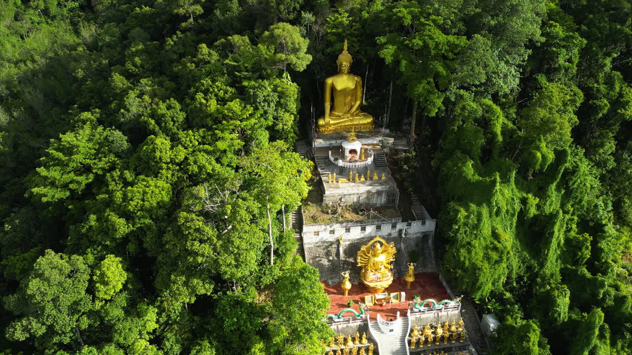 tomada aérea de arriba hacia abajo del templo de buda de la montaña dorada rodeado de árboles verdes a la luz del sol - ao nang, tailandia