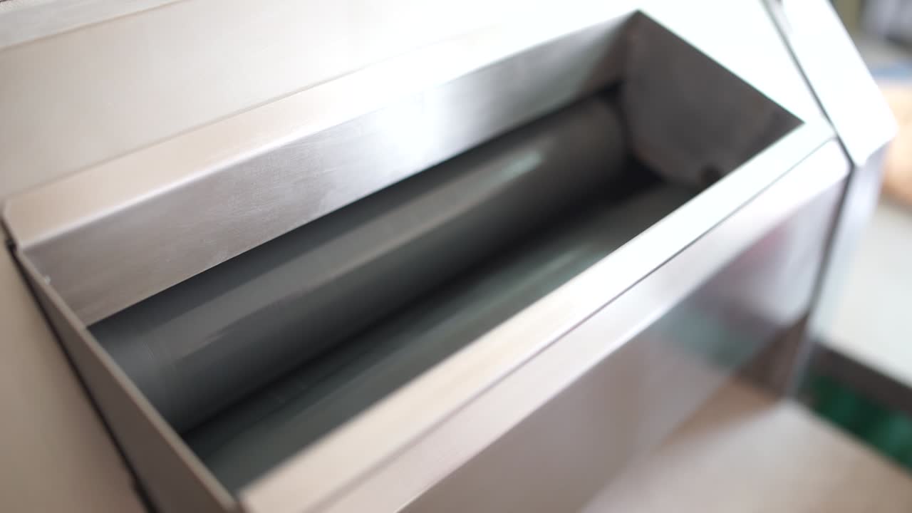 primer plano de las manos dejando caer la masa en la parte superior de una máquina enrolladora de pan industrial