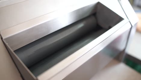 close-up of hands dropping dough into the top of an industrial bread roller machine